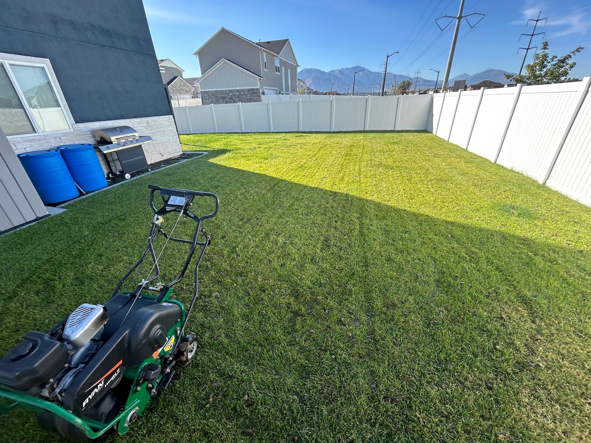 Person mowing grass on a red zero-turn riding lawnmower in a grassy yard near buildings.