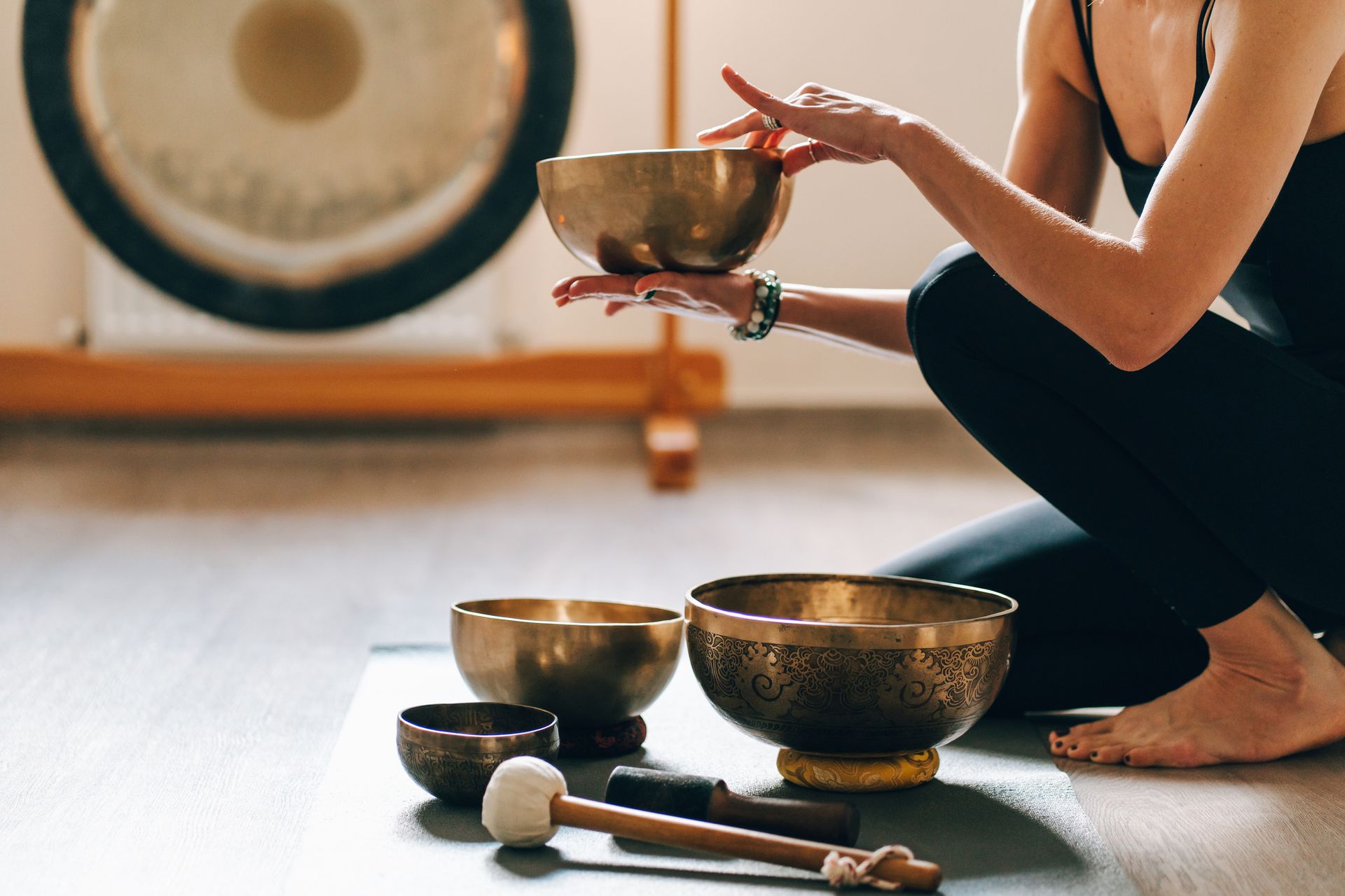 A woman is kneeling on the floor playing a singing bowl. A woman is kneeling on the floor playing a singing bowl.