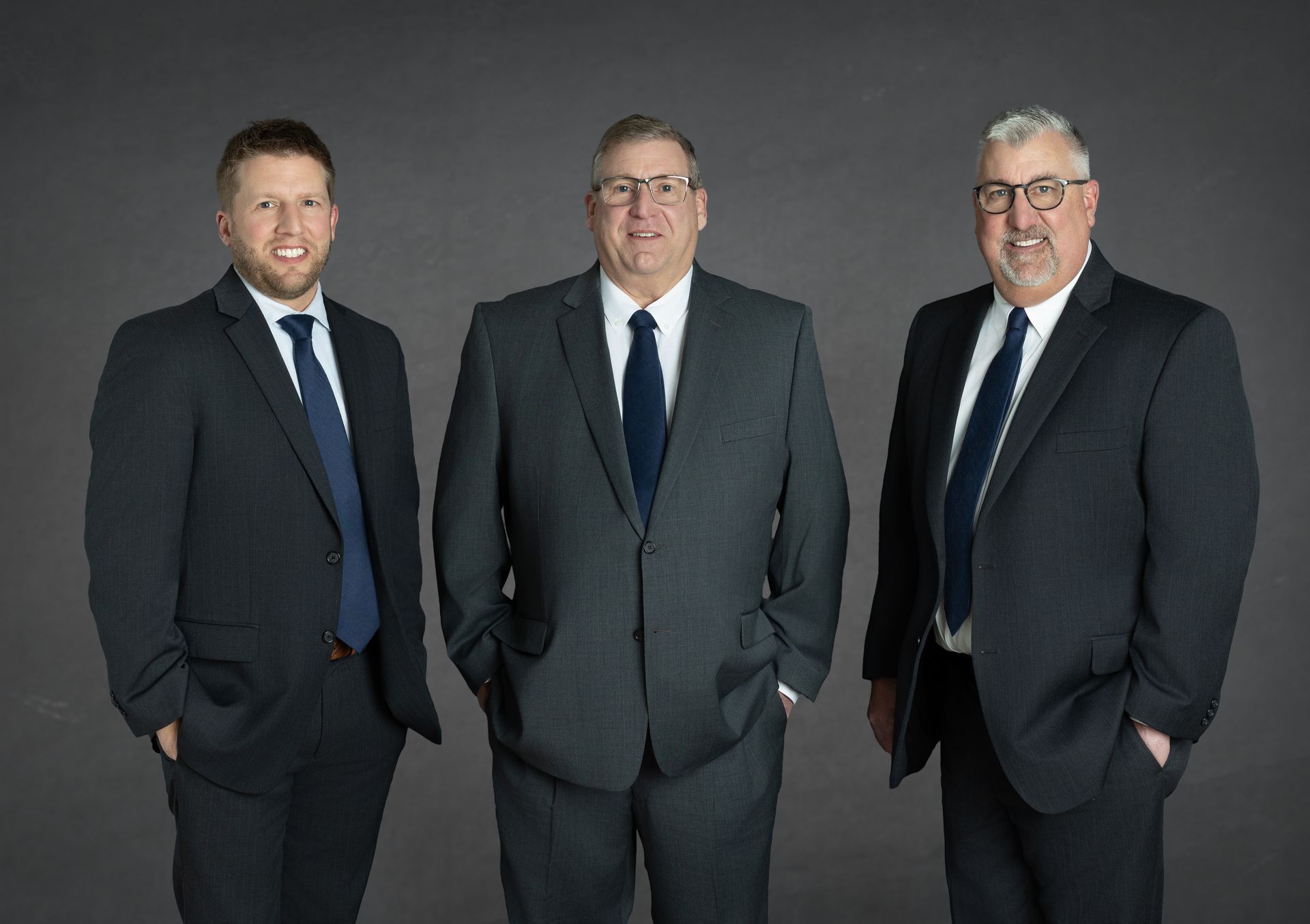 Portrait of Robert, Larry, Terry and Larry Jr. Schildmeyer in gray suits and red striped ties, standing in front of a staircase.