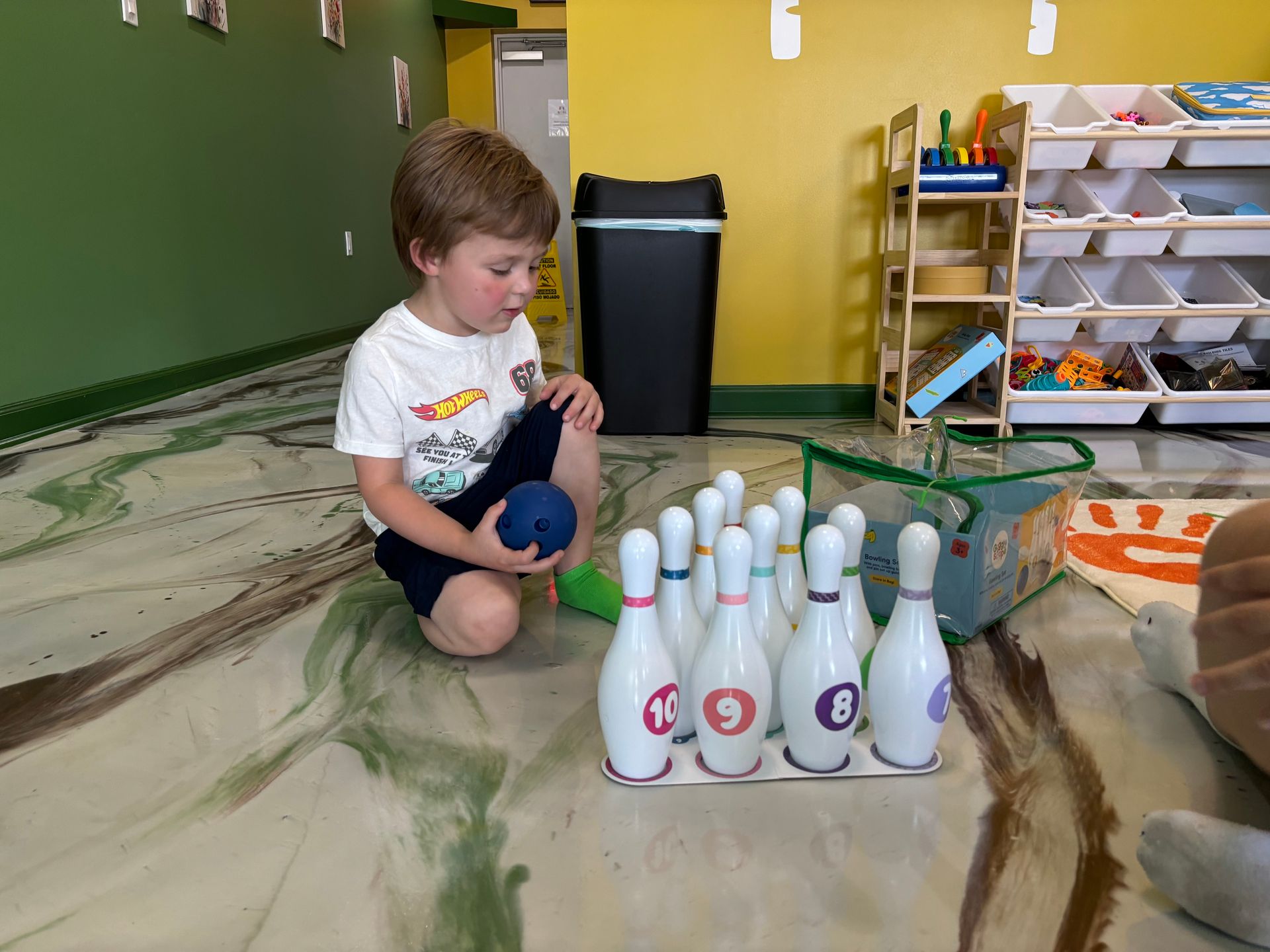A little girl wearing glasses is playing with paint on a table.