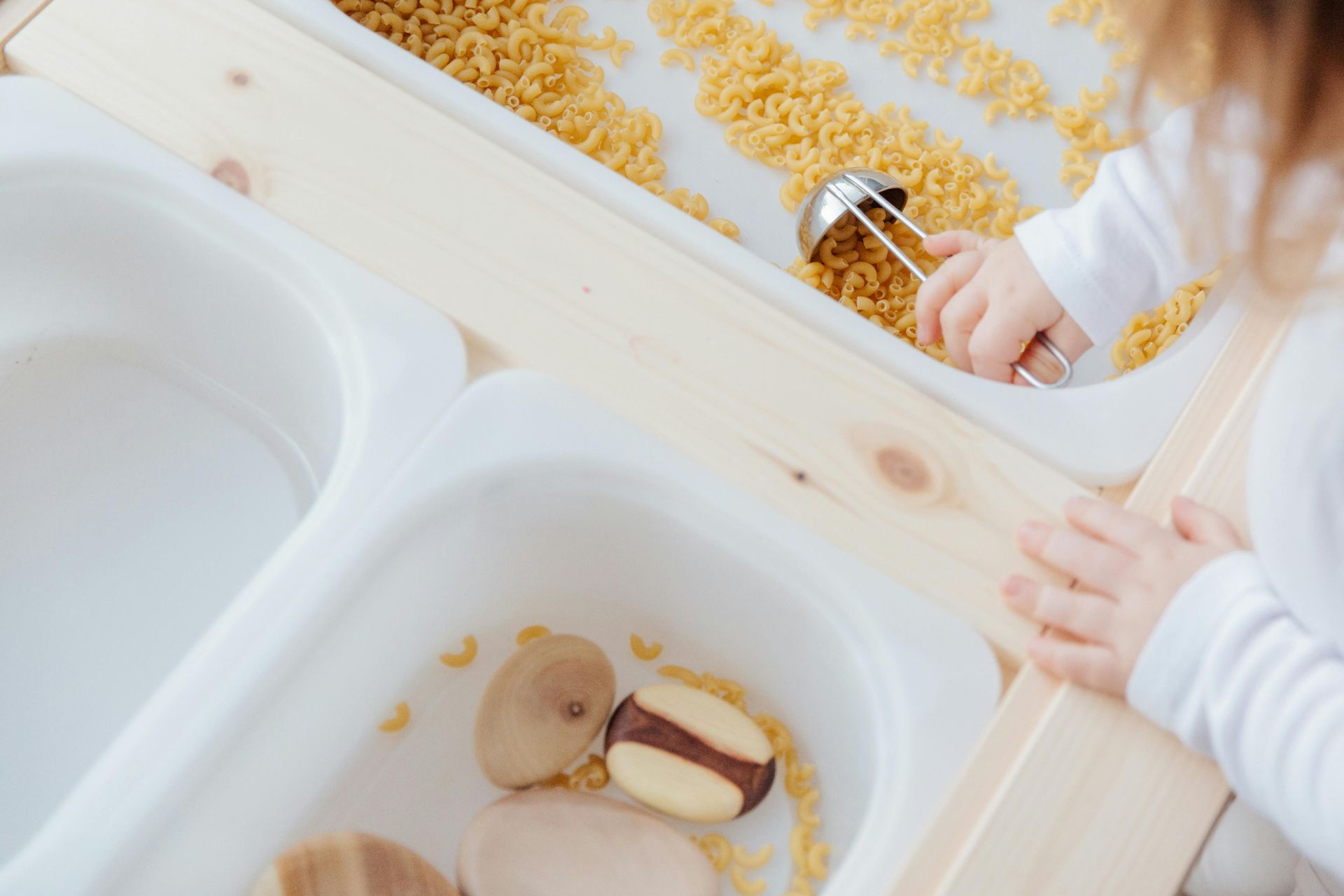 A child is playing with macaroni and cheese in a sensory bin.