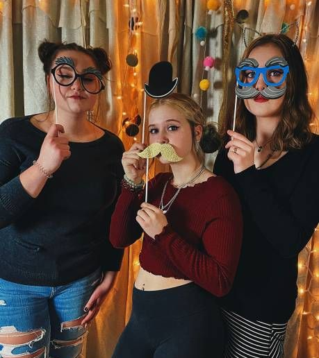 Women holding mustache and glasses photo booth props.