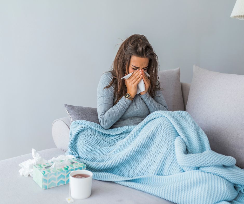 Person resting on a couch under a blanket with tissues, feeling unwell from flu symptoms.