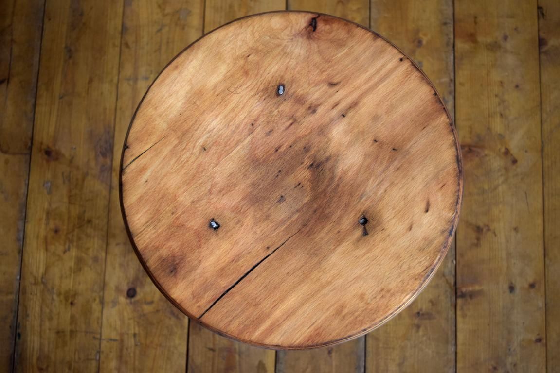 Nahaufnahme einer runden Sitzfläche aus massivem Buchenholz eines antiken Werkstatthockers mit markanten Rissen und erzählender Patina.