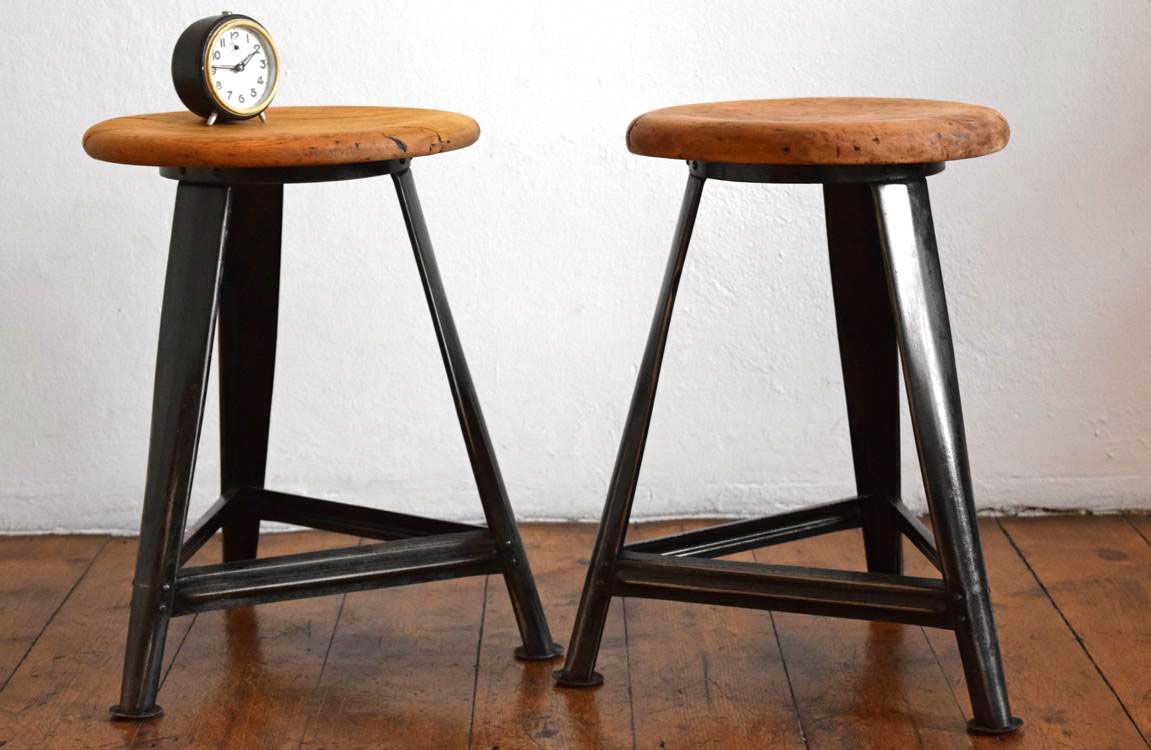 Zwei antike Werkstatthocker aus Stahl und Holz mit Uhrmacher-Wecker, mitteldeutsches Industriedesign in heller Wohnumgebung.“