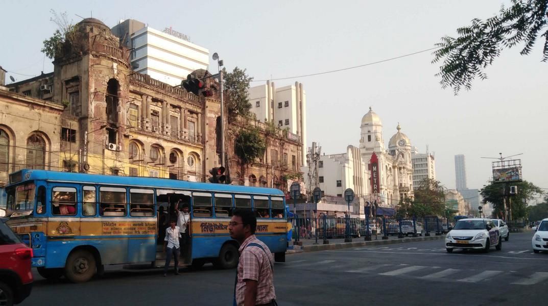 Blick über Esplanada in Kalkutta, Menschen steigen in einen alten Bus, dahinter  historisches Metro-Kino und Metropolitan Building