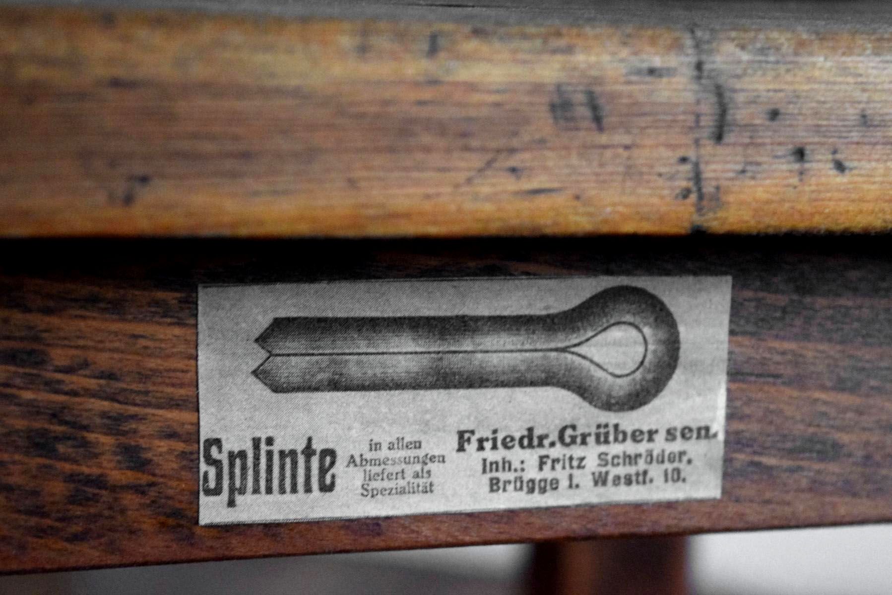 Detailansicht eines antiken Werkstatthockers mit historischem Typografie-Etikett der Firma Friedr. Grüber sen. für Splinte, Illustration der funktionalen Sachlichkeit