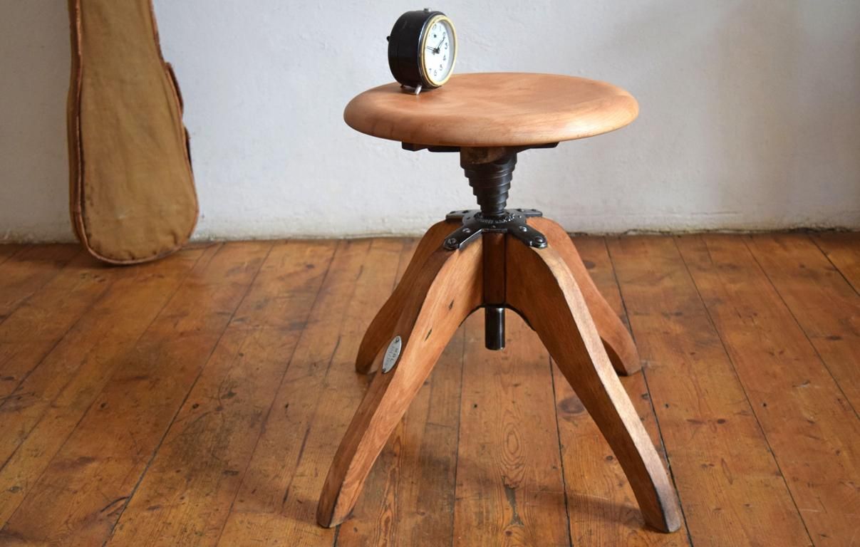 Antiker Werkstatthocker mit massiver eiserner Gewindespindel auf Dielenboden, hölzernes Dreibein-Gestell als Symbol für mechanische Dauerhaftigkeit ohne Verfallsdatum.