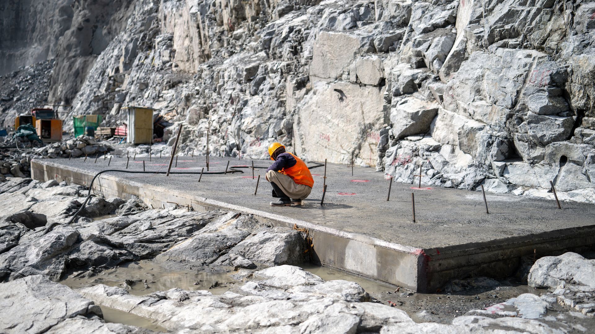 Worker inspecting a concrete foundation slab at a rocky job site.