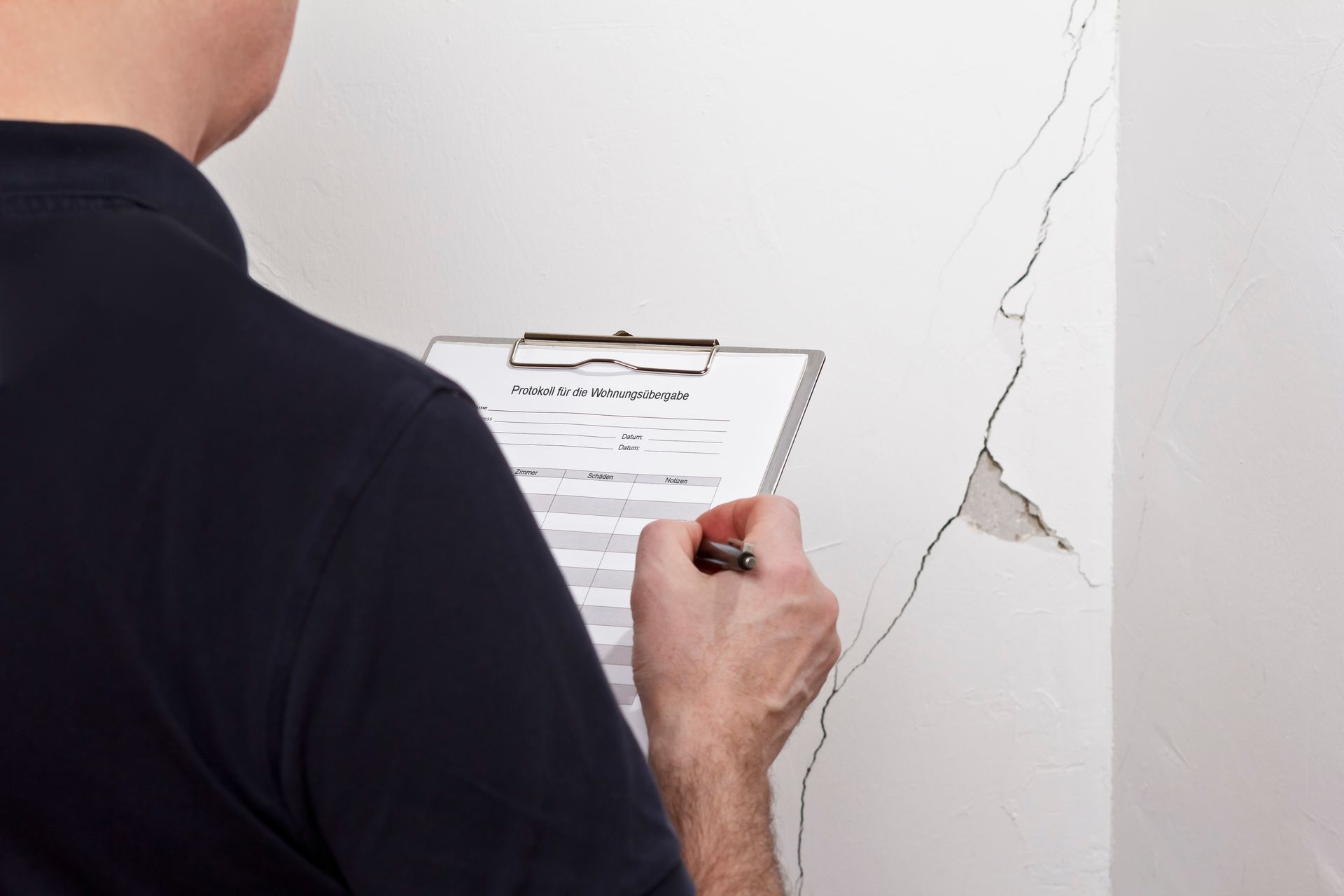 Technician performing foundation inspection while documenting wall cracks on interior surface.