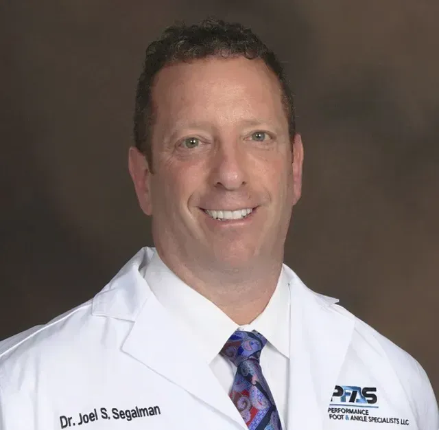 A smiling doctor in a lab coat with a stethoscope around his neck.