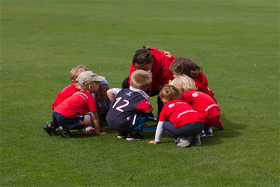 A group of children in red soccer jerseys are kneeling in a huddle on a field.