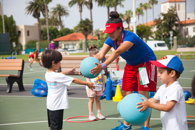A woman is teaching two children how to play with balls on a tennis court.