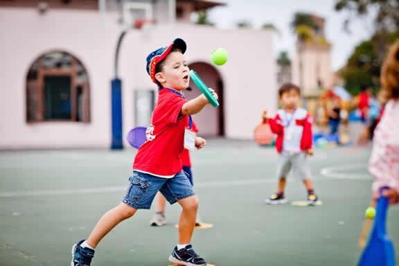 A young boy is playing with a tennis ball on a court.