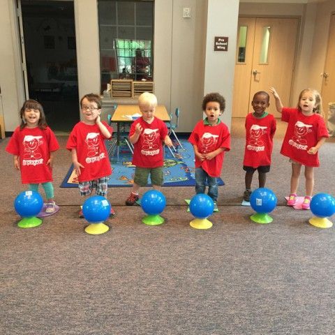 A group of children wearing red shirts are standing next to blue balls on a carpet.