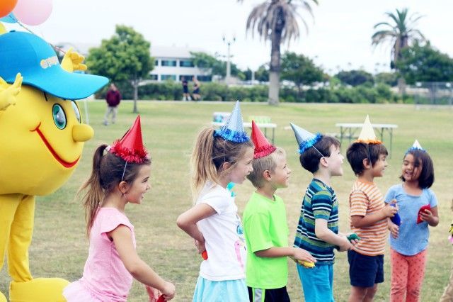 A group of children wearing party hats are standing next to a yellow mascot.