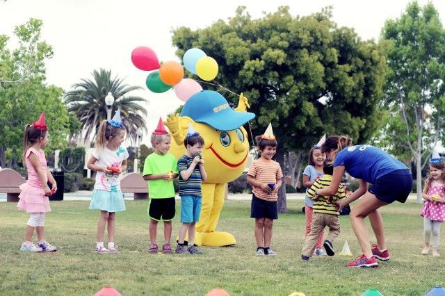 A group of children are playing with a mascot in a park