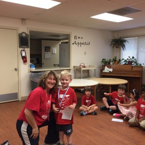 A woman in a red shirt is standing next to a boy in a red shirt with a medal around his neck.