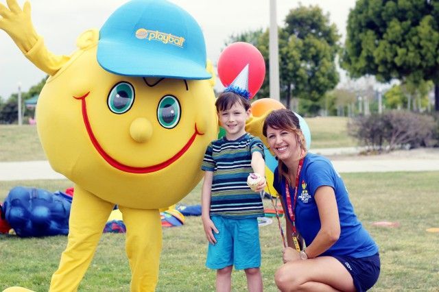 A woman kneeling next to a yellow smiley face mascot