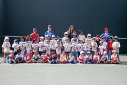 A large group of children are posing for a picture on a tennis court.