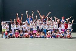 A large group of children are posing for a picture on a tennis court.