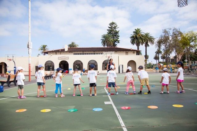 A group of children are standing on a basketball court in front of a building.