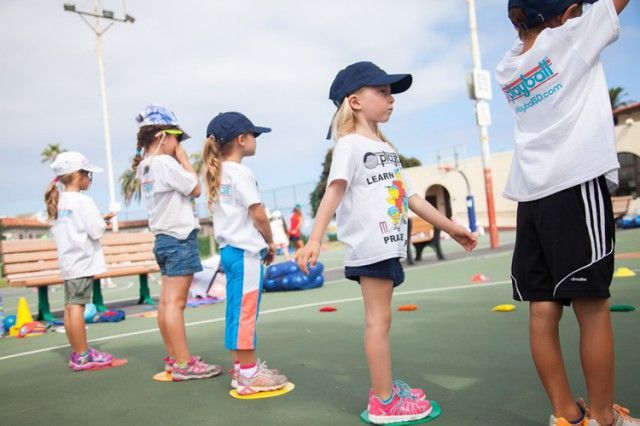 A group of young children are standing on a tennis court.