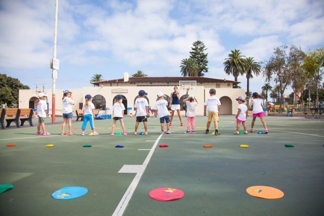A group of children are standing in a row on a tennis court.