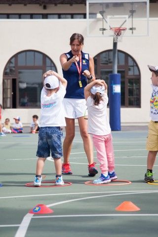 A woman is standing next to a group of children on a basketball court.