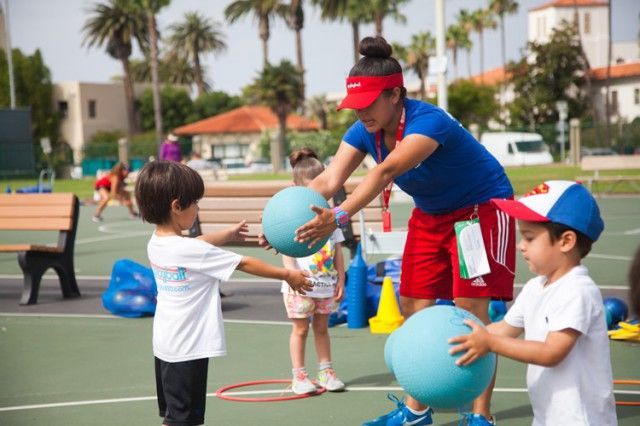 A woman is teaching two children how to play with balls on a tennis court.