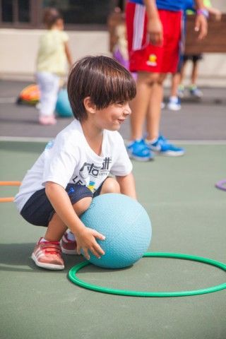 A young boy is squatting down next to a blue ball and a green hoop.