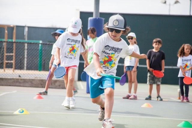 A group of children are playing tennis on a tennis court.