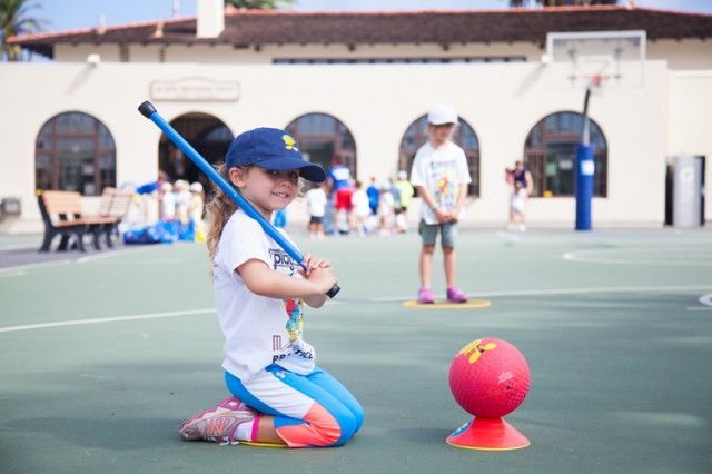 A little girl is kneeling down with a bat and a ball.