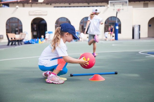 A little girl is playing with a ball on a court.
