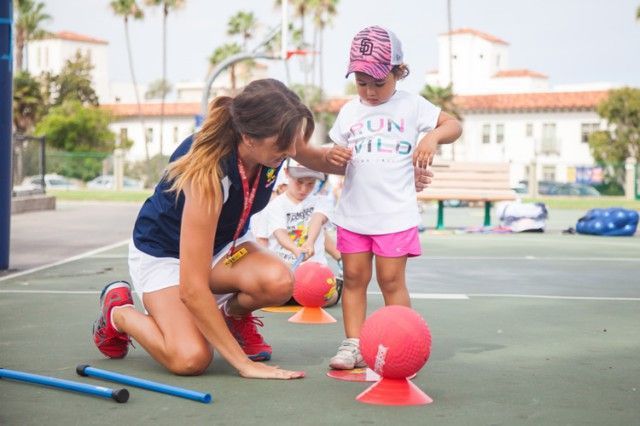 A woman is kneeling down next to a little girl on a court.