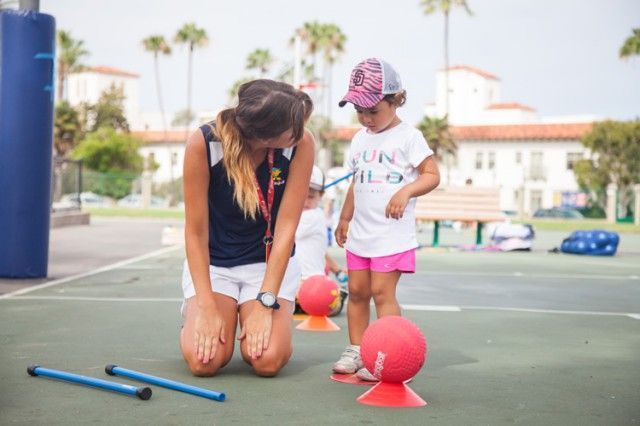 A woman is kneeling down next to a little girl on a court.