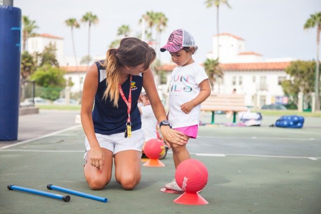 A woman is kneeling down next to a little girl on a tennis court.