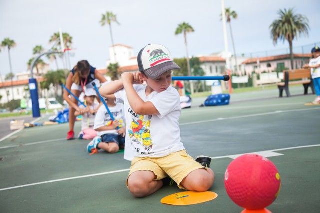 A young boy wearing a california hat is kneeling down on a basketball court.
