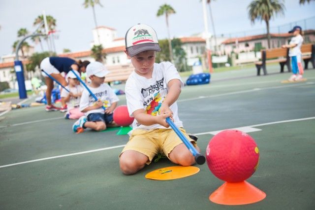 A young boy is playing with a ball and a stick on a court.