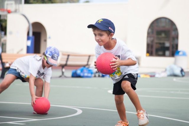 A boy and a girl are playing with balls on a basketball court.