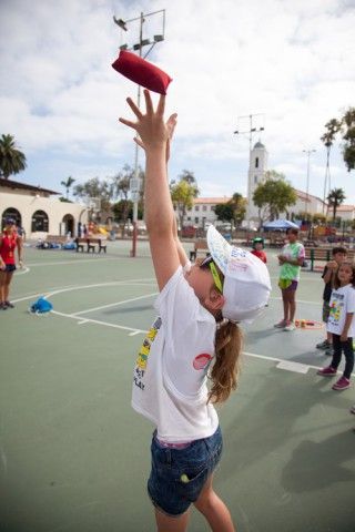 A young girl is throwing a frisbee in the air on a court.