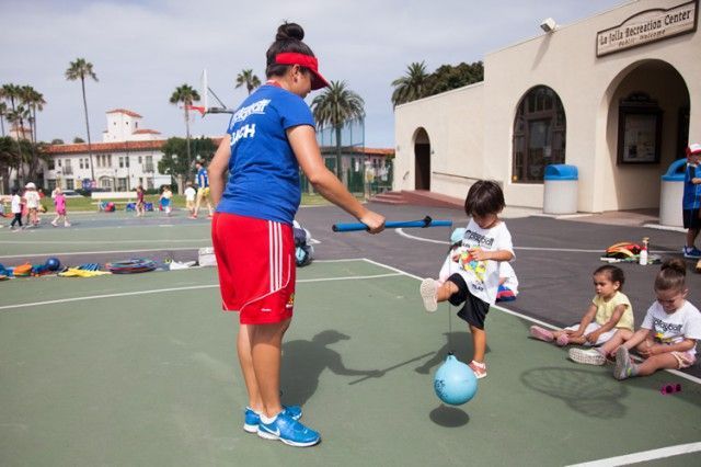 A woman in a blue shirt is teaching a child how to kick a soccer ball