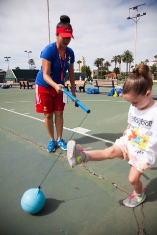 A woman and a little girl are playing with a ball on a tennis court.