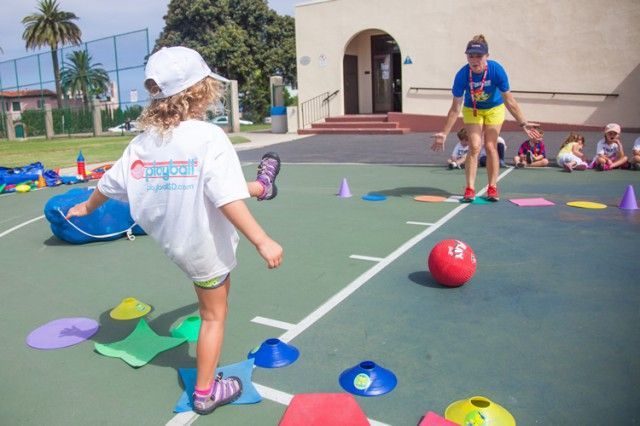 A little girl is kicking a ball on a tennis court