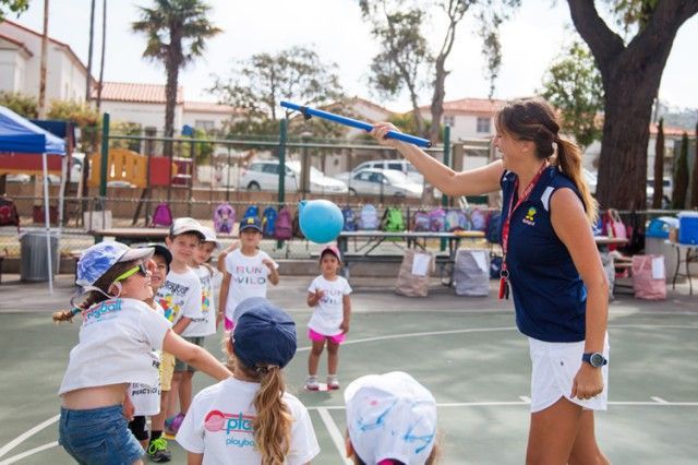A group of children are playing a game with a woman holding a stick.