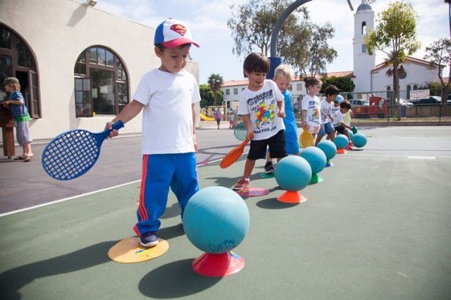 A boy in a superman hat is holding a tennis racquet
