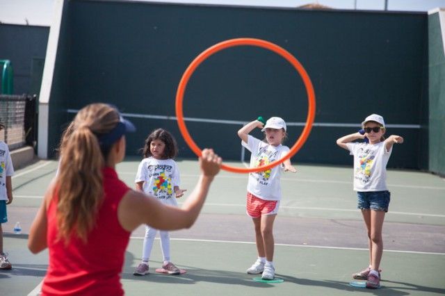 A group of children are playing with a hula hoop on a tennis court.