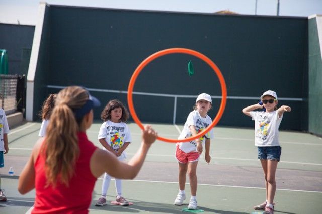 A group of children are playing with a hula hoop on a tennis court