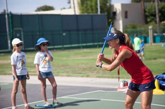 A woman is teaching two young girls how to play tennis on a court.