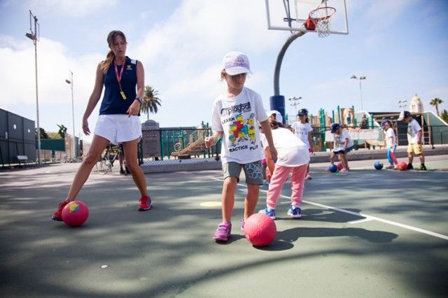 A group of children are playing with balls on a basketball court.